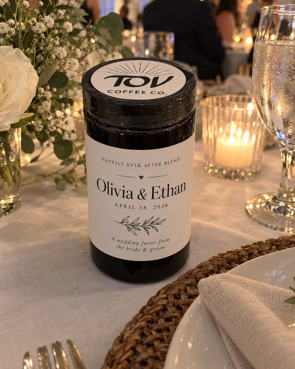 A Tov glass coffee jar standing on a candlelit table setting, its label reading Happily Ever After Blend, Olivia and Ethan. An illustrative mockup, not a photograph of a past event.